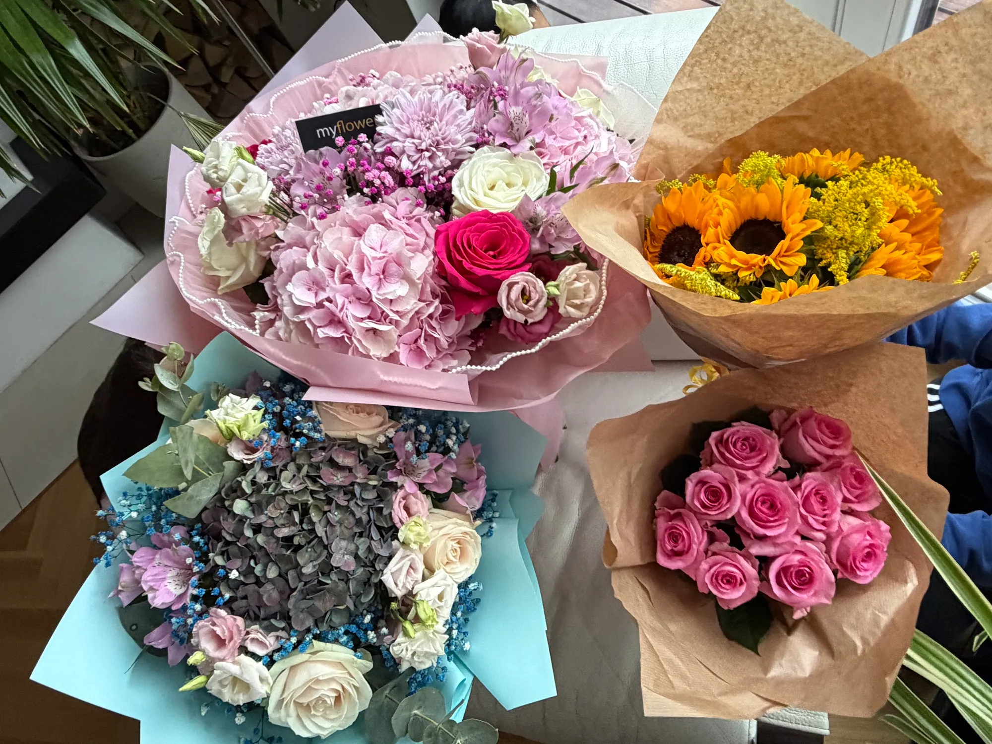 Vier Sträuße auf einem Tisch: Hortensien mit Rosen, Sonnenblumen, pinke Rosen und ein blau-weißer Strauß